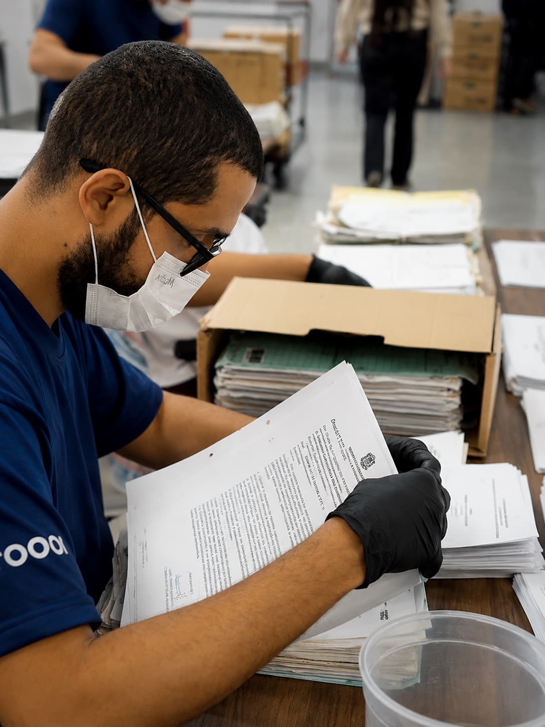 Analista da SOS Docs, de luvas e máscara, conferindo processo a processo o conteúdo de uma caixa do acervo